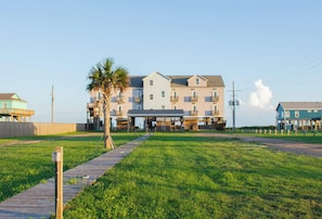 A beachfront hotel with multiple floors, a covered walkway, and a palm tree.