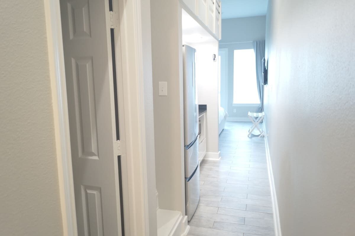 A hallway with a door, a refrigerator, and a window with curtains.
