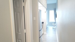 Un passadís amb una porta, un frigorífic i una finestra amb cortines.