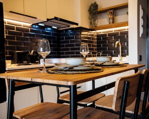 A modern kitchen with a wooden table set for two, featuring a bowl, wine glasses, and cutlery. - San Eugenio Apartments by Andes STR (Ñuñoa)