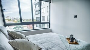 Ein Schlafzimmer mit einem großen Fenster, einem Bett mit Kissen und einem Tablett mit einer Kaffeemaschine.