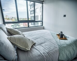 A bedroom with a large window, a bed with pillows, and a tray with a coffee maker. - San Eugenio Apartments by Andes STR (Ñuñoa)