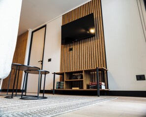 Una sala moderna con un televisor de pantalla plana montado en una pared de madera, una mesa de centro redonda y una estantería llena de libros.