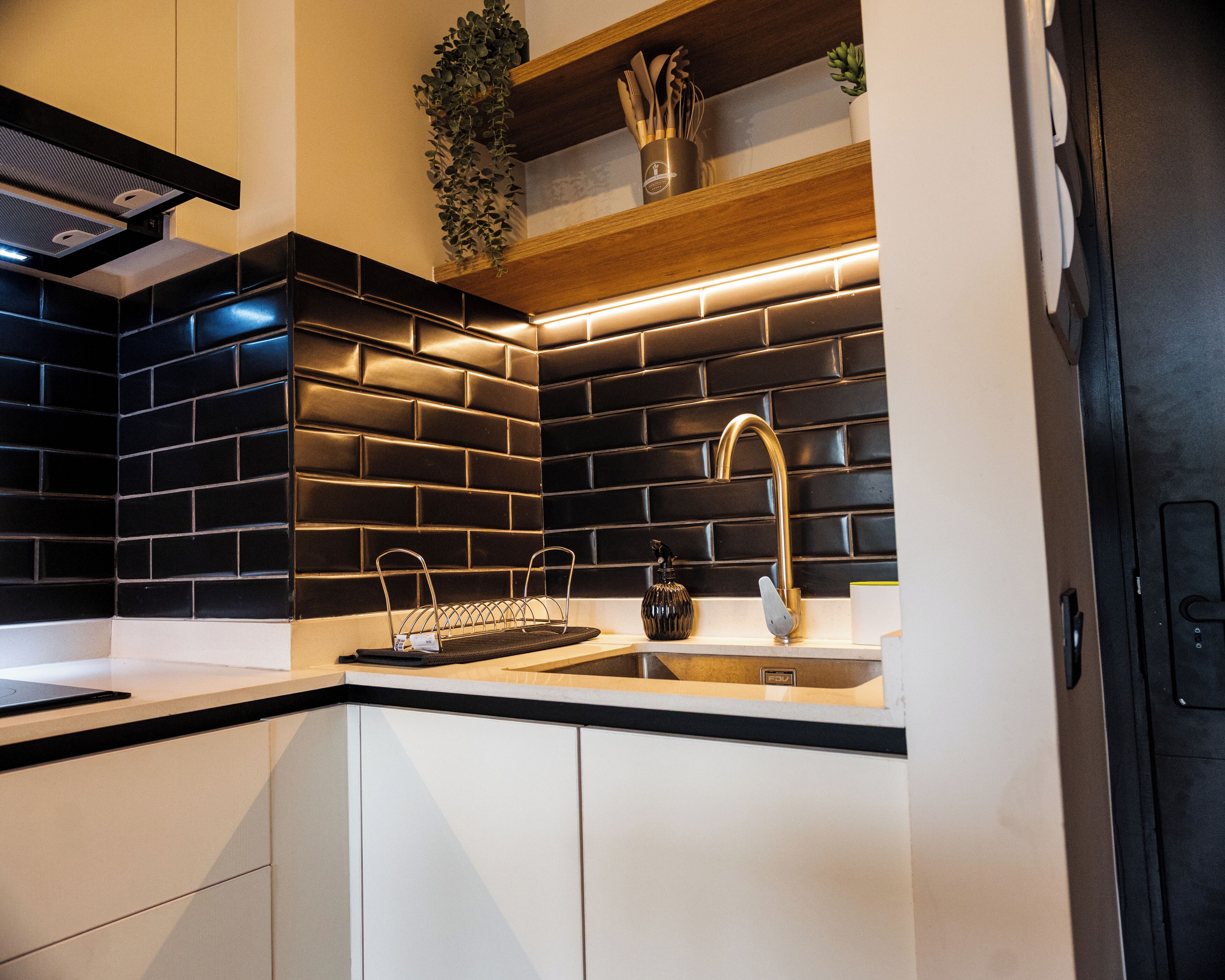 Une cuisine moderne avec un dosseret de carreaux noirs, un évier en acier inoxydable et des étagères en bois.