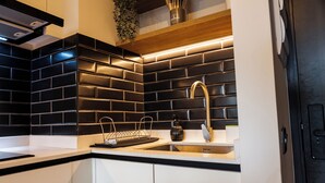 Eine moderne Küche mit schwarzem Fliesenrückwand, Edelstahl-Spüle und Holzregalen.