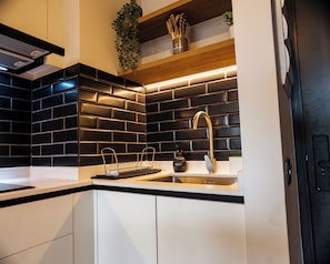 A modern kitchen with black tiled backsplash, stainless steel sink, and wooden shelves. - San Eugenio Apartments by Andes STR (Ñuñoa)