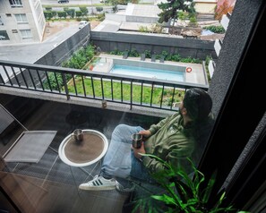 A person sitting on a balcony with a view of a swimming pool, a chair, and a small table with a cup and saucer. - San Eugenio Apartments by Andes STR (Ñuñoa)