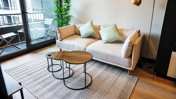 Ein modernes Wohnzimmer mit einer Couch, zwei Beistelltischen, einer Stehlampe und Blick auf einen Balkon.