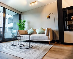 A modern living room with a sofa, a coffee table, a floor lamp, and a large window. - San Eugenio Apartments by Andes STR (Ñuñoa)