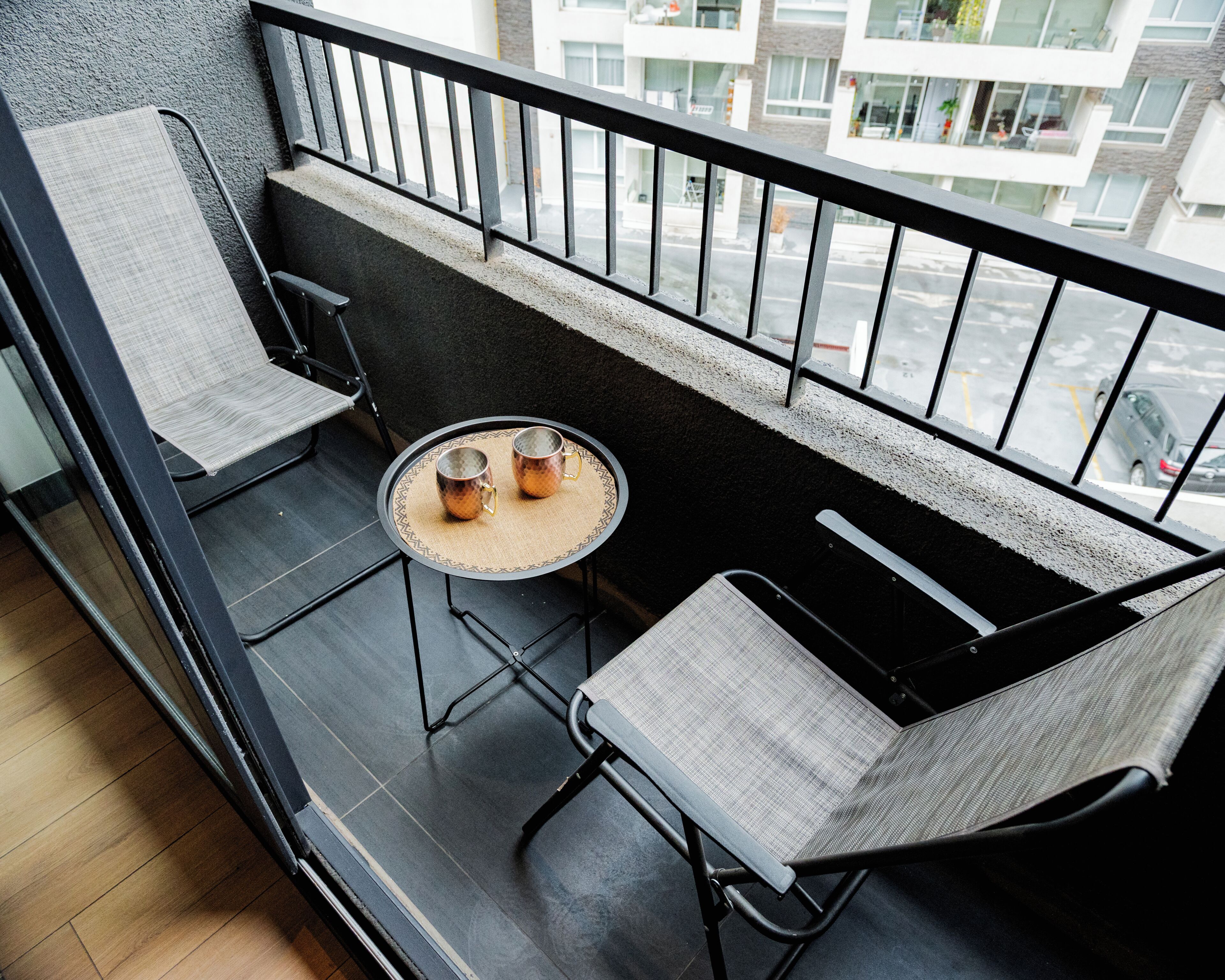 Ein Balkon mit zwei Stühlen, einem kleinen runden Tisch und einem Getränk.