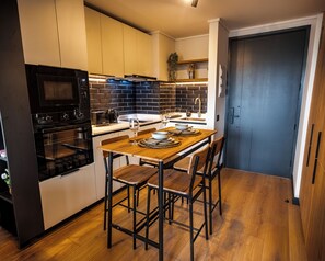A modern kitchen with a wooden dining table, black chairs, and a built-in oven. - San Eugenio Apartments by Andes STR (Ñuñoa)