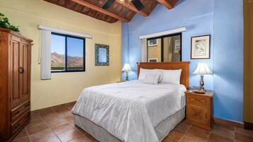 A bedroom with a bed, bedside tables, a wooden wardrobe, a window with a view, and a ceiling fan.