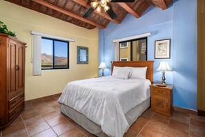 Une chambre à coucher comprenant un lit, des tables de chevet, une armoire en bois, une fenêtre avec vue et un ventilateur de plafond.