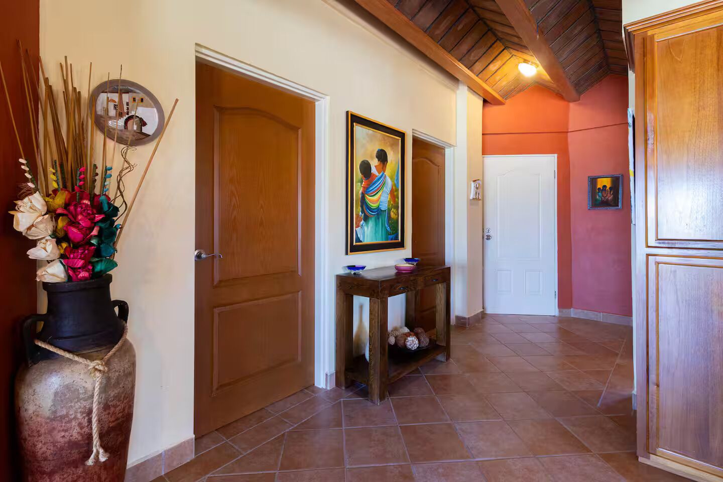 Un couloir avec des portes en bois, un tableau accroché au mur et une petite table sur laquelle sont posés des bols.