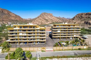 Un hôtel à plusieurs étages, doté de balcons, d’un parking et offrant une vue sur les montagnes.