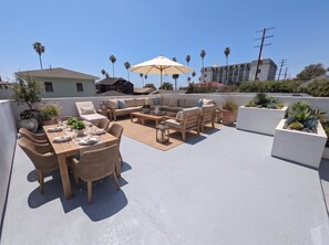 A rooftop patio with outdoor furniture, a dining table set, and potted plants. - Bluff Park Oasis (Long Beach)