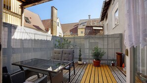 Un patio con una mesa de vidrio, sillas de mimbre y plantas en macetas.