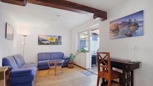 Una sala de estar con un sofá azul, una mesa de comedor de madera y una silla, y un cuadro con un paisaje de montaña.