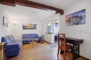 A living room with a blue sofa, a wooden dining table with a chair, and a painting of a mountain landscape. - Pet-Friendly Apartment in Historic Tanner’s House with Private Terrace in the Allgäu (Memmingen)