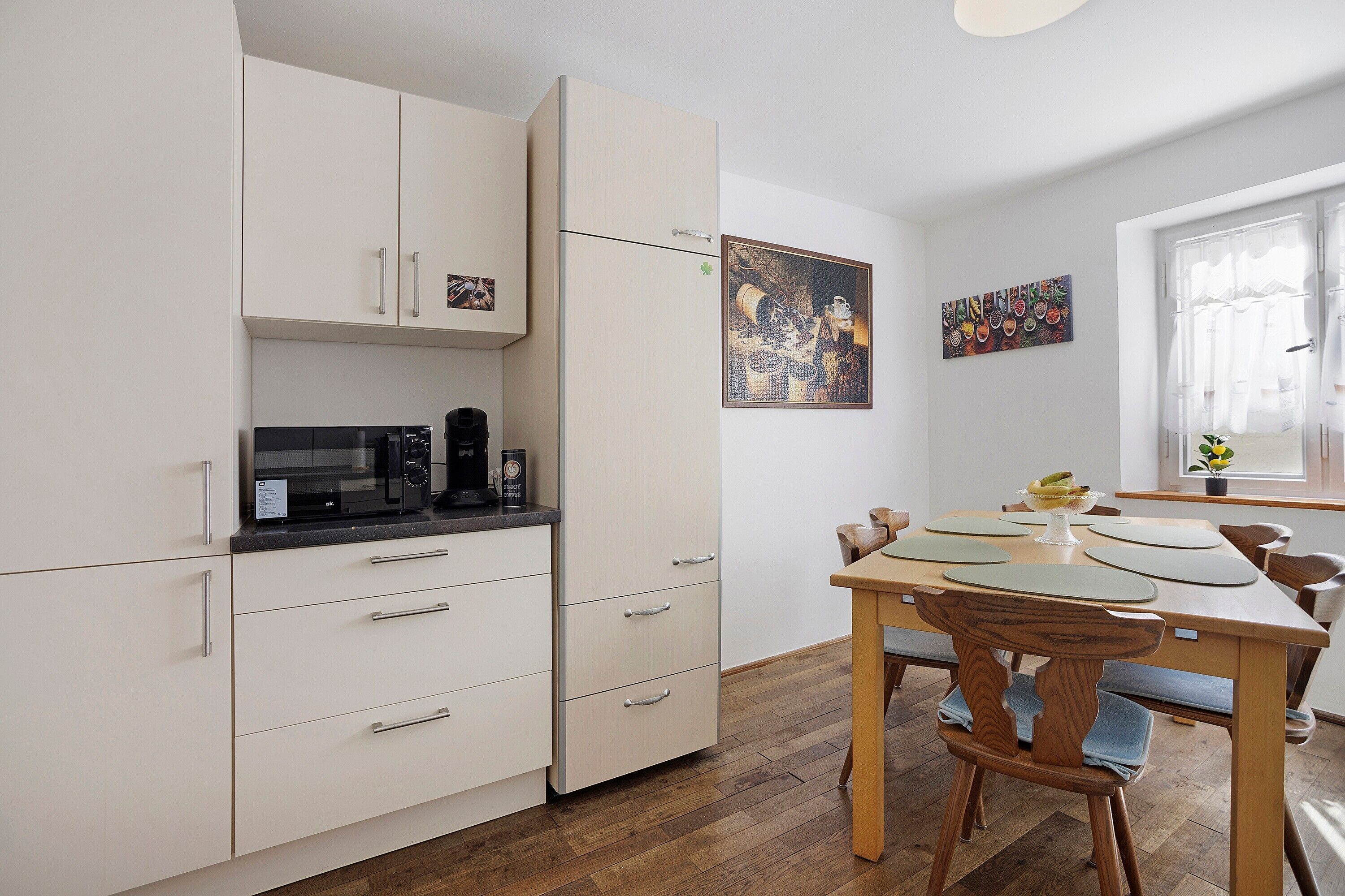 Una cocina moderna con armarios blancos, una cafetera negra y una mesa de comedor con sillas.