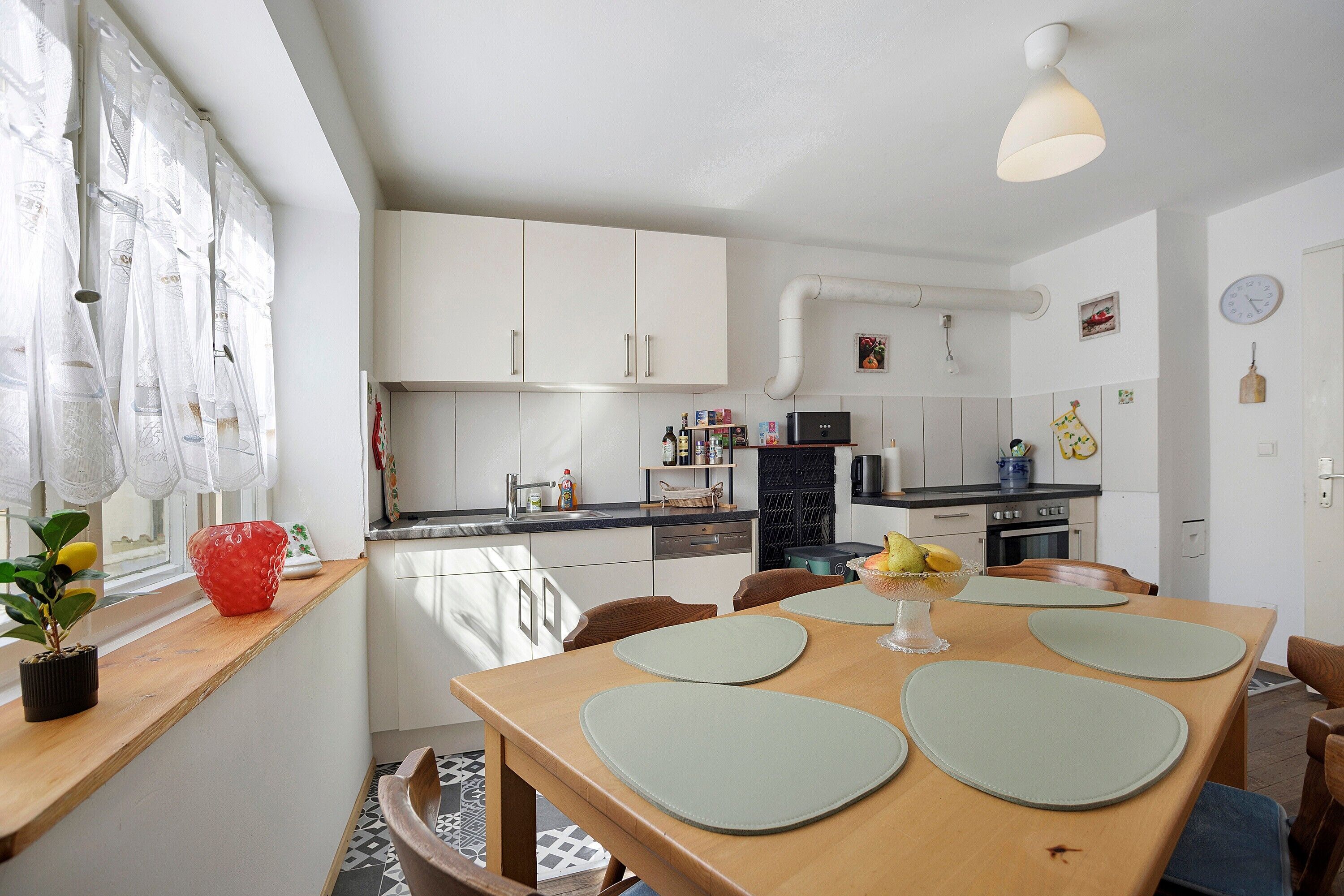 Eine moderne Küche mit weißen Schränken, einem schwarzen Kühlschrank und einem Essbereich mit einem Holztisch und Stühlen.