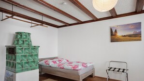 Un dormitorio con una cama, un mueble verde para guardar objetos, un cuadro y una silla de metal.