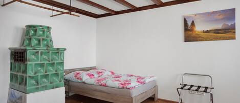 A bedroom with a bed, a green storage unit, a painting, and a metal chair.