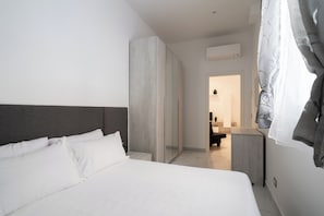 Ein modernes Hotelzimmer mit einem großen Bett, einem Kleiderschrank und einem durchgehenden Türbogen sichtbaren Badezimmer.