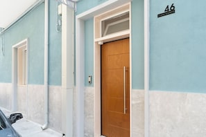 Ein Gebäude mit zwei Türen, eine mit einer Holzvertäfelung und die andere mit einer Glasscheibe. An der Wand befindet sich die Zahl '46' und ein kleines Schild über der Tür.