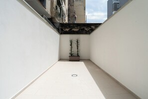 Um corredor estreito com piso de azulejos, um vaso de planta e uma grelha de escoamento visível.