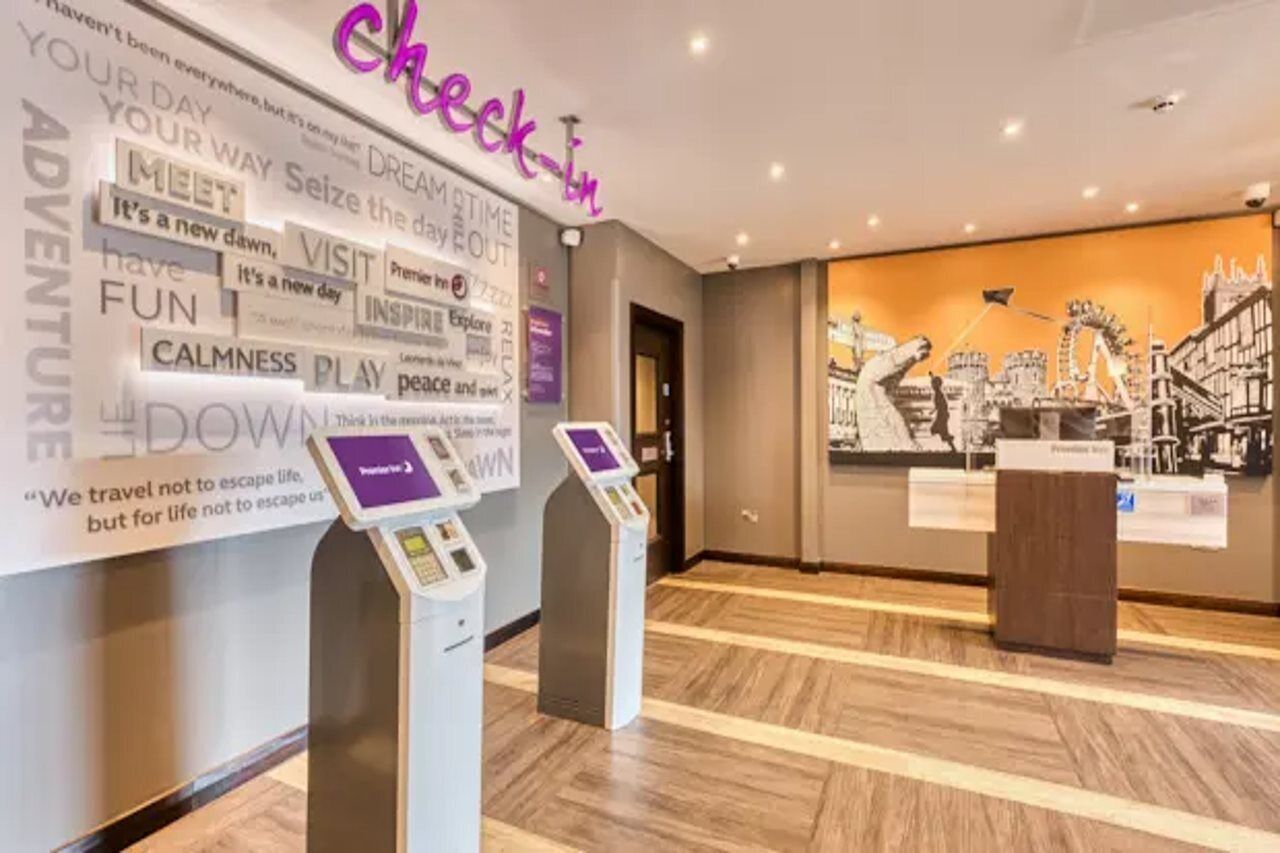 A hotel reception area with a 'check-in' desk, a digital kiosk, and a wall with motivational phrases and a cityscape mural.