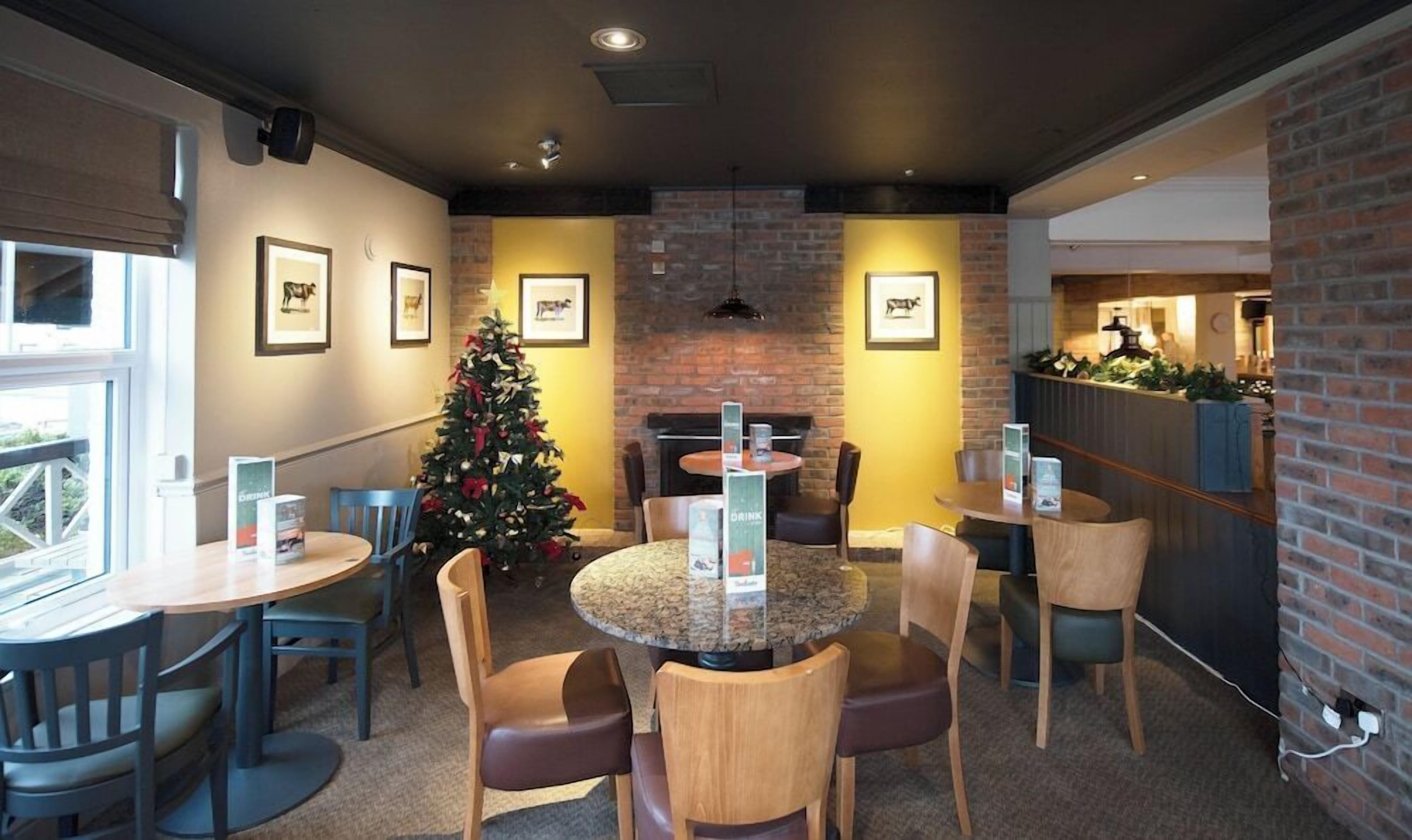 A cozy dining area with round tables and chairs, a brick wall, and framed pictures on the wall.