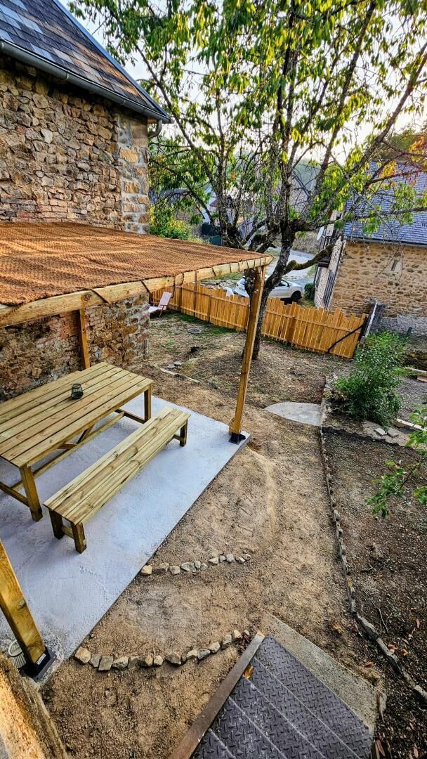 Un patio con mesa y banco de madera, un muro de piedra y una zona cercada.