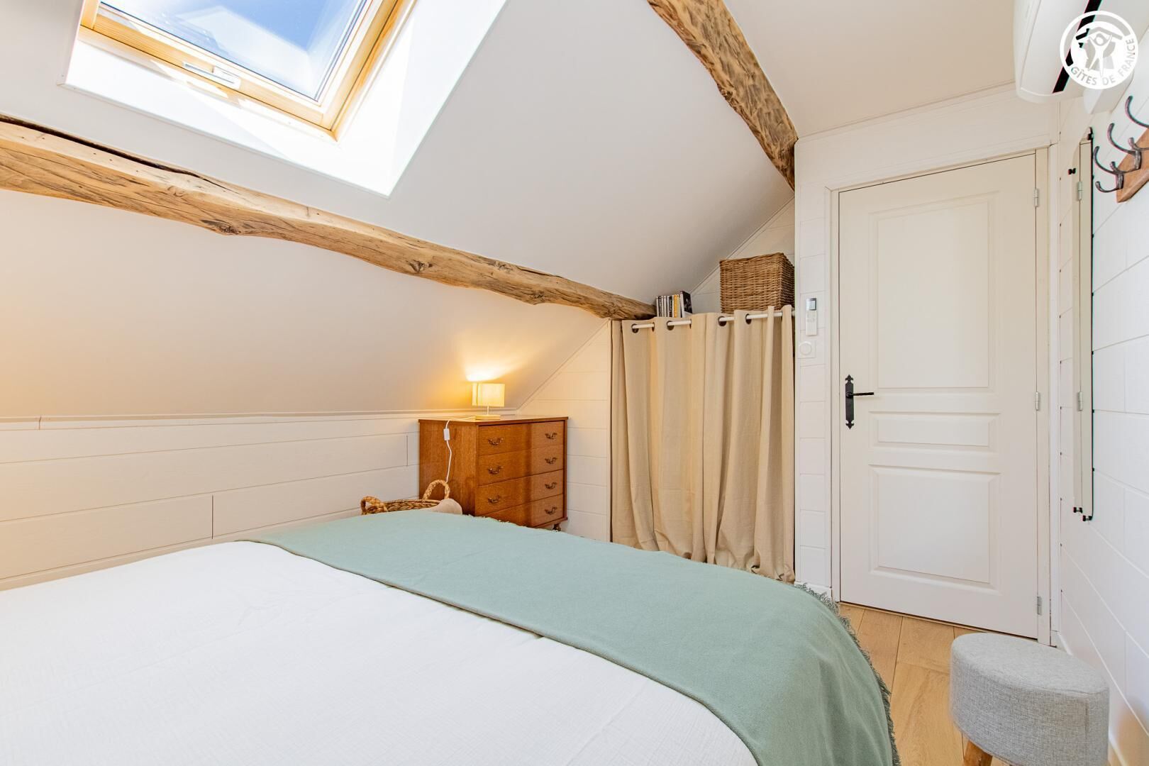 A bedroom with a skylight, a bed, a dresser, a nightstand, and a door.