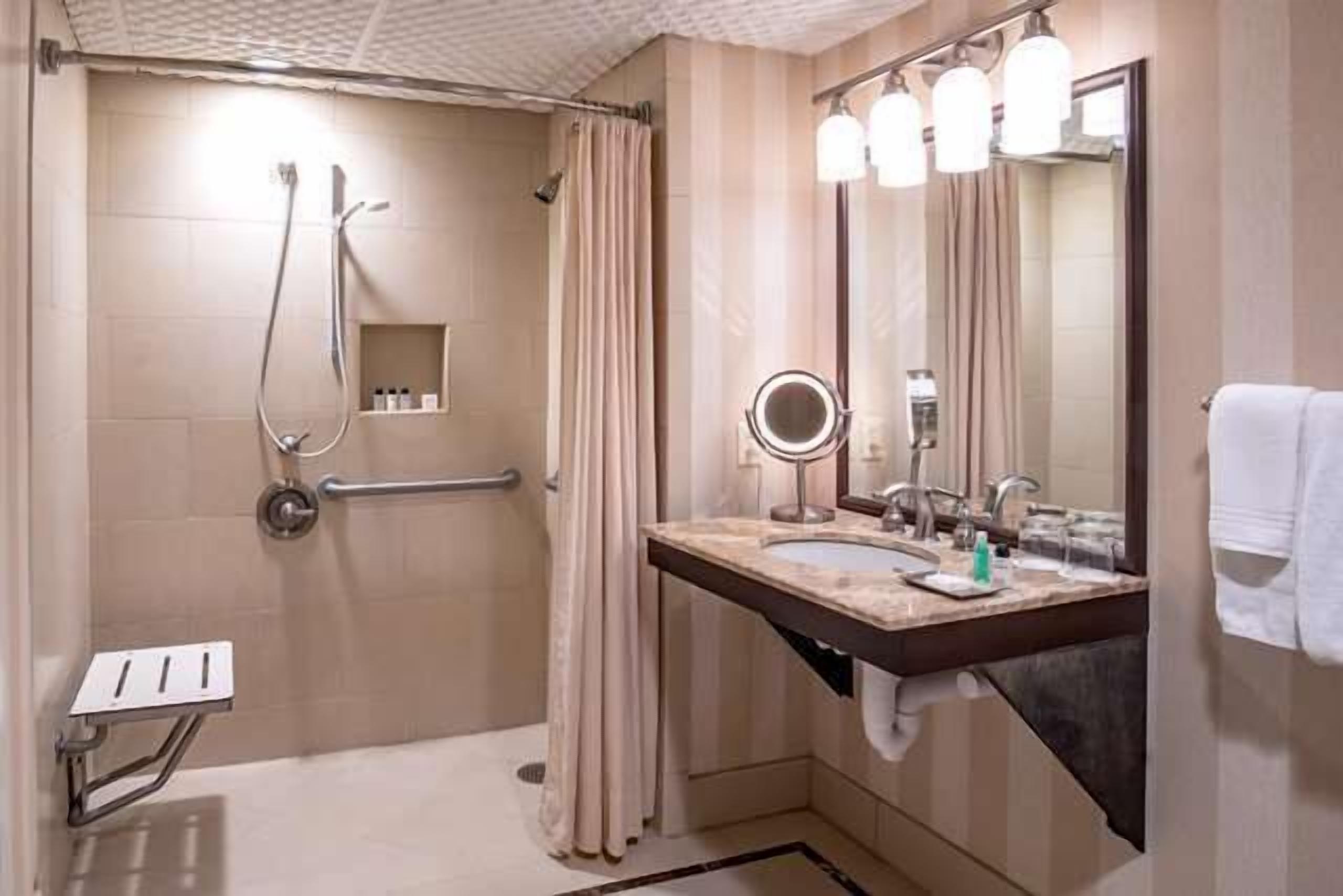 Un baño con ducha, lavamanos, espejo y toallero.