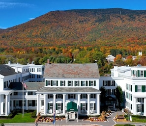 A large white building with a central entrance and green shutters, surrounded by a well-maintained lawn and a mountain backdrop. - ADA King Room w/ Roll-In Shower & Views (Manchester)