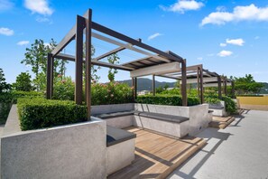 An outdoor seating area with concrete planters, wooden benches, and a pergola structure. - Laguna Beachside 2BR Apartment near Bang Tao Beach (Choeng Thale)