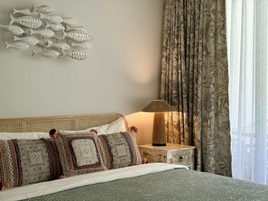 Uma cama bem arrumada com almofadas estampadas, uma decoração de peixe na parede, um abajur e uma cortina floral.