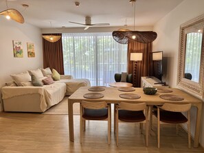 A modern living room with a sofa, dining table, chairs, and a ceiling fan. - Laguna Beachside 2BR Apartment near Bang Tao Beach (Choeng Thale)