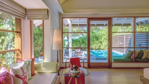 Une pièce avec une table en verre, une chaise rouge, un canapé et une vue sur une piscine.