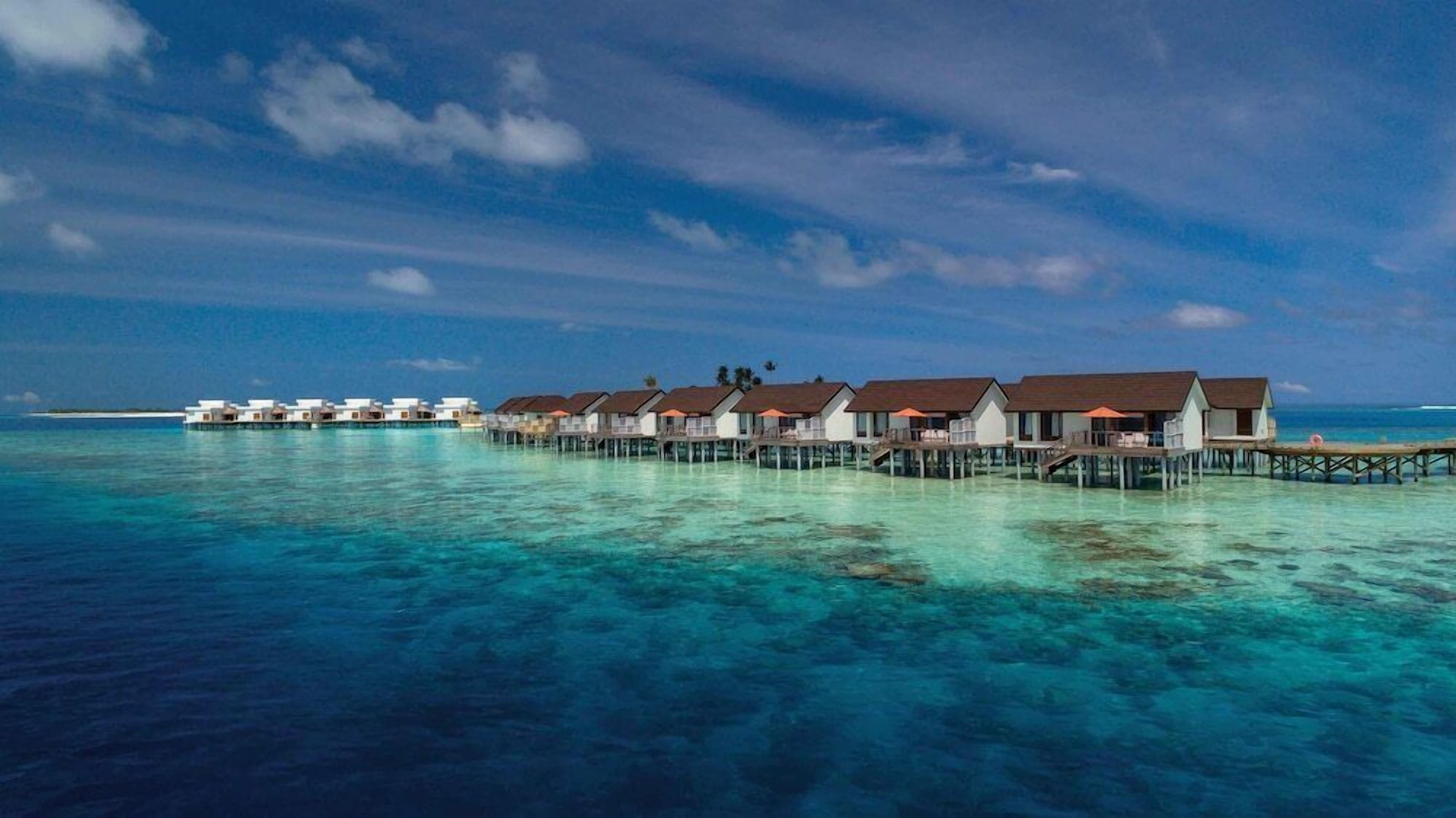 Overwater bungalows connected by wooden walkways over clear turquoise water.