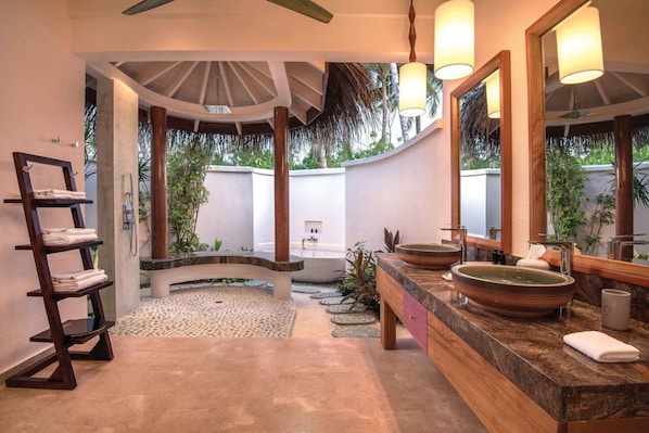 A bathroom with a bathtub, two sinks, a shelf with towels, and a large mirror.