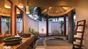 Une salle de bain avec deux grands lavabos ovales, une baignoire, un banc en bois, un porte-serviettes et un chemin en pierre.