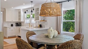 Uma cozinha moderna com armários brancos, uma mesa de jantar redonda com cadeiras de vime e uma grande luminária pendente trançada.