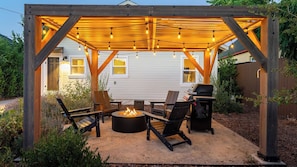 A covered outdoor seating area with a fire pit, chairs, and string lights. - Lavender Porch by Avantstay Designer Bungalow + Fire Pit Near Downtown, Paso (Paso Robles)