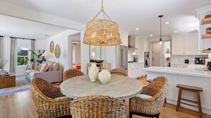A modern kitchen with white cabinets, a round dining table with wicker chairs, and a hanging rattan chandelier. - Lavender Porch by Avantstay Designer Bungalow + Fire Pit Near Downtown, Paso (Paso Robles)