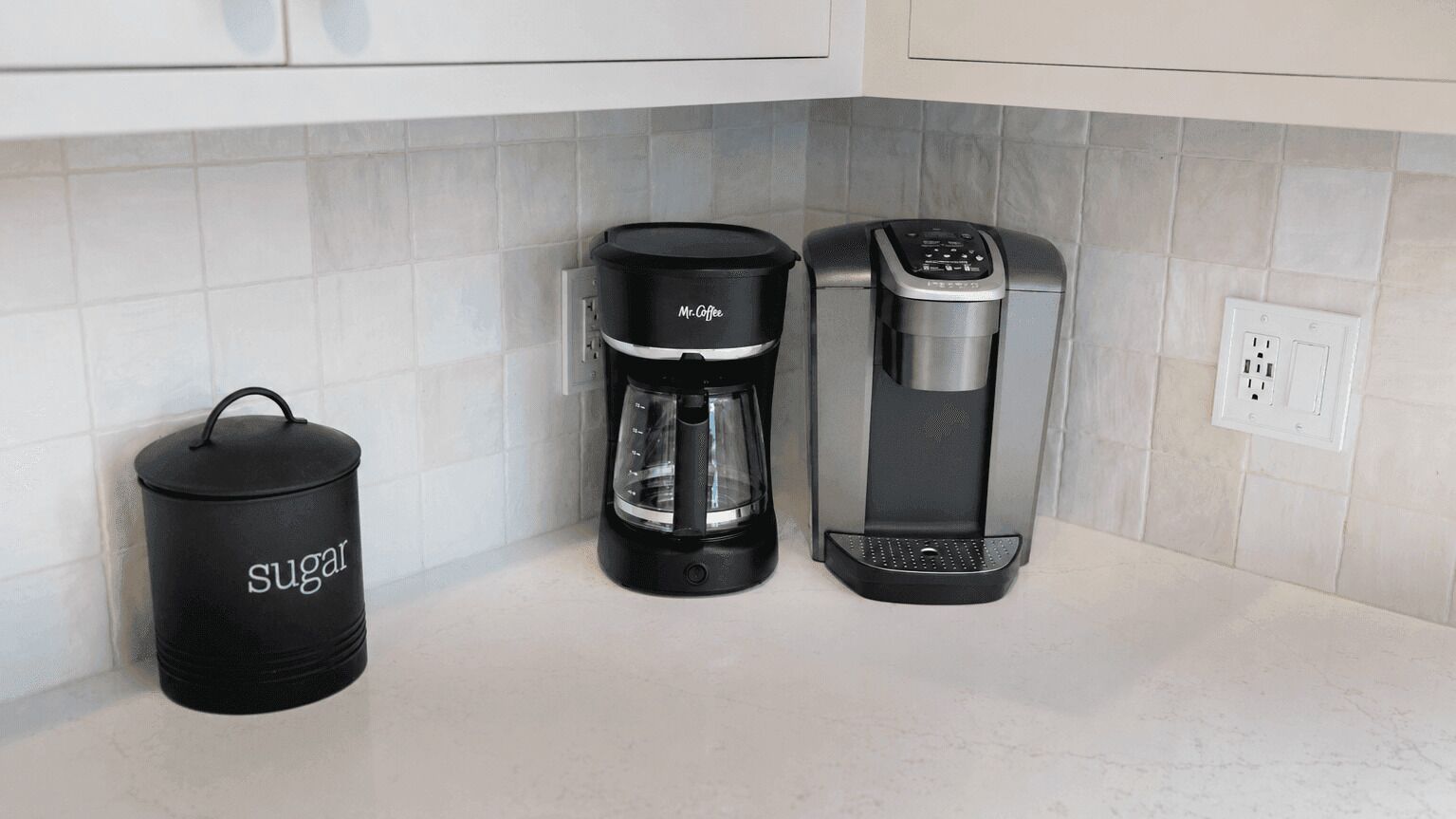 A kitchen with a coffee maker, a sugar container, and a power outlet.