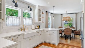 Une cuisine moderne avec des meubles blancs, un îlot central intégré et un coin repas doté de chaises en osier.