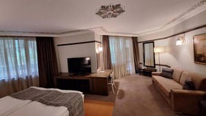 Ett hotellrum med en säng, ett skrivbord, en tv, en soffa och en stor spegel.