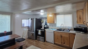 Cocina compacta con refrigerador, estufa, lavavajillas y microondas. Cuenta con una mesa de comedor con sillas y un banco.